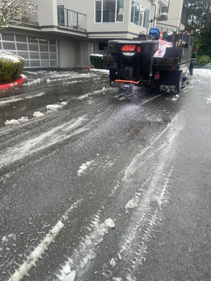 Jireh truck spreading material on a slushy drive lane beside a residential building in Western Washington