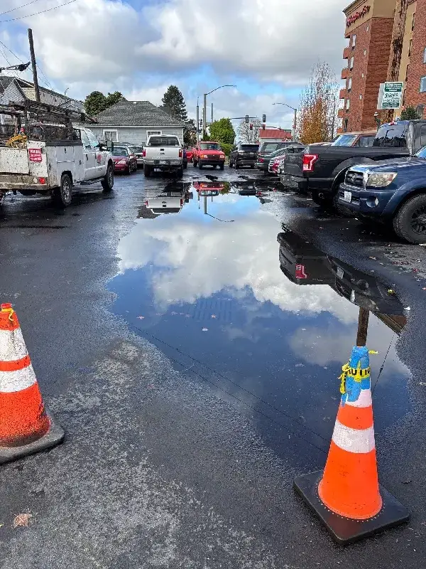Parking lot with ponding water around a storm drain and safety cones before catch basin cleaning