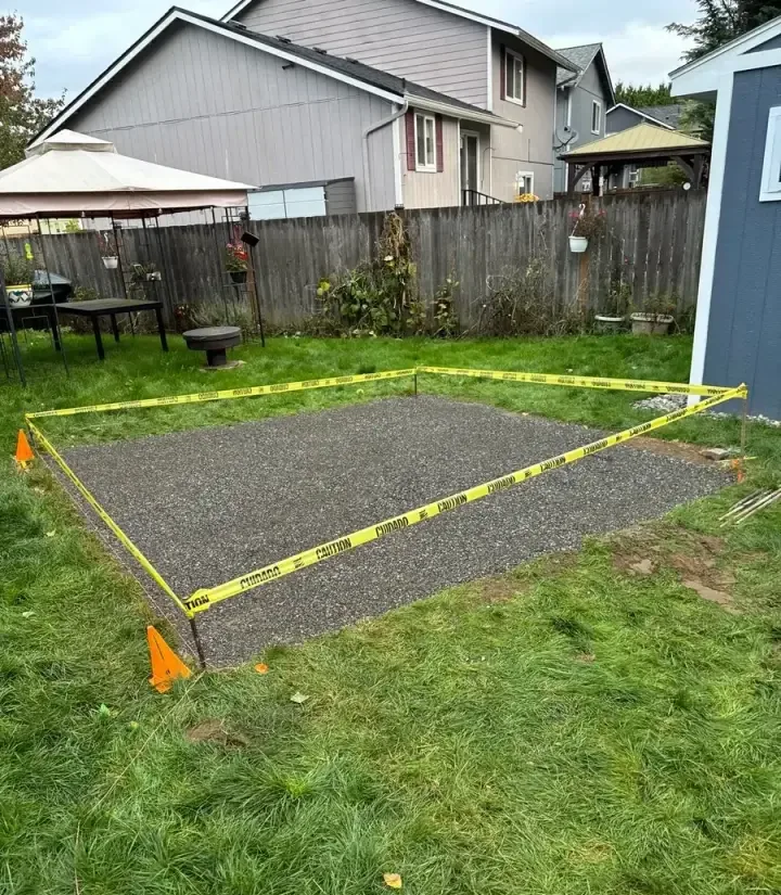 Compacted aggregate base for a paver patio, staked out with caution tape in a backyard in late October in Snohomish County